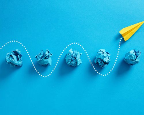 Gelbes Papierflugzeug auf blauem Hintergrund.